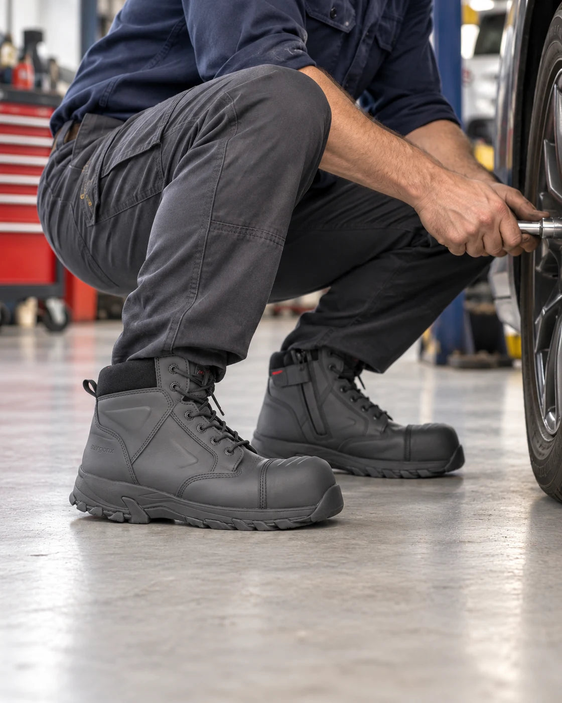 Mechanic crouching beside a stationary car while wearing Helium Black boots on a workshop floor